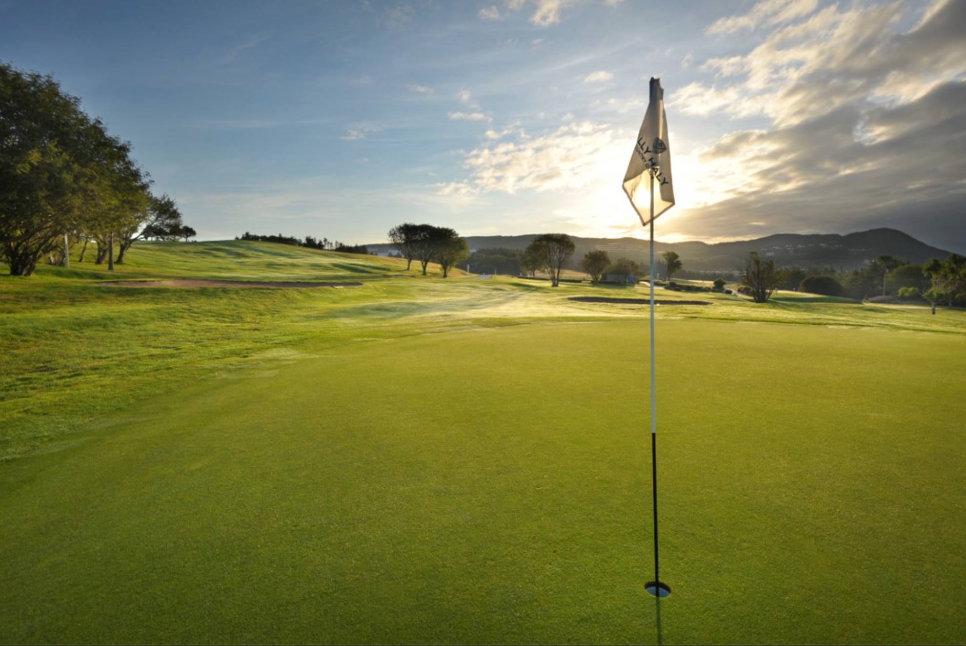 Bally Haly Golf Course green at sunrise with flagstick, rolling fairway and distant hills.
