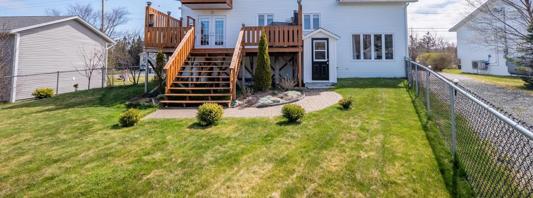 Spacious backyard in Flatrock with a fenced lawn, garden landscaping, and large wooden deck
