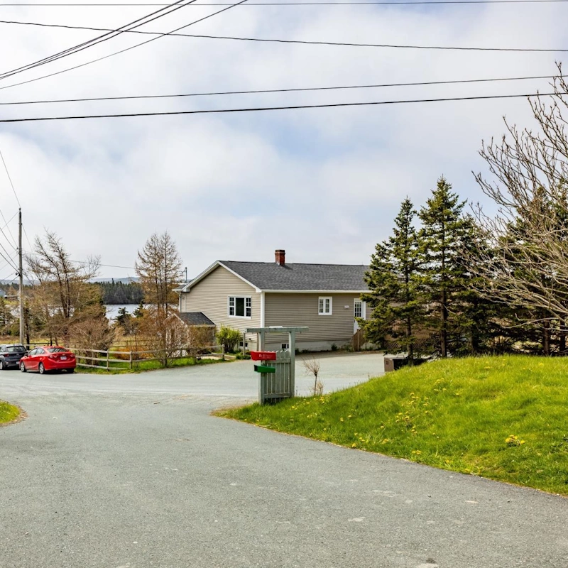 Residential street view in Portugal Cove–St. Philip's featuring a single-family home, trees, and partial water views.