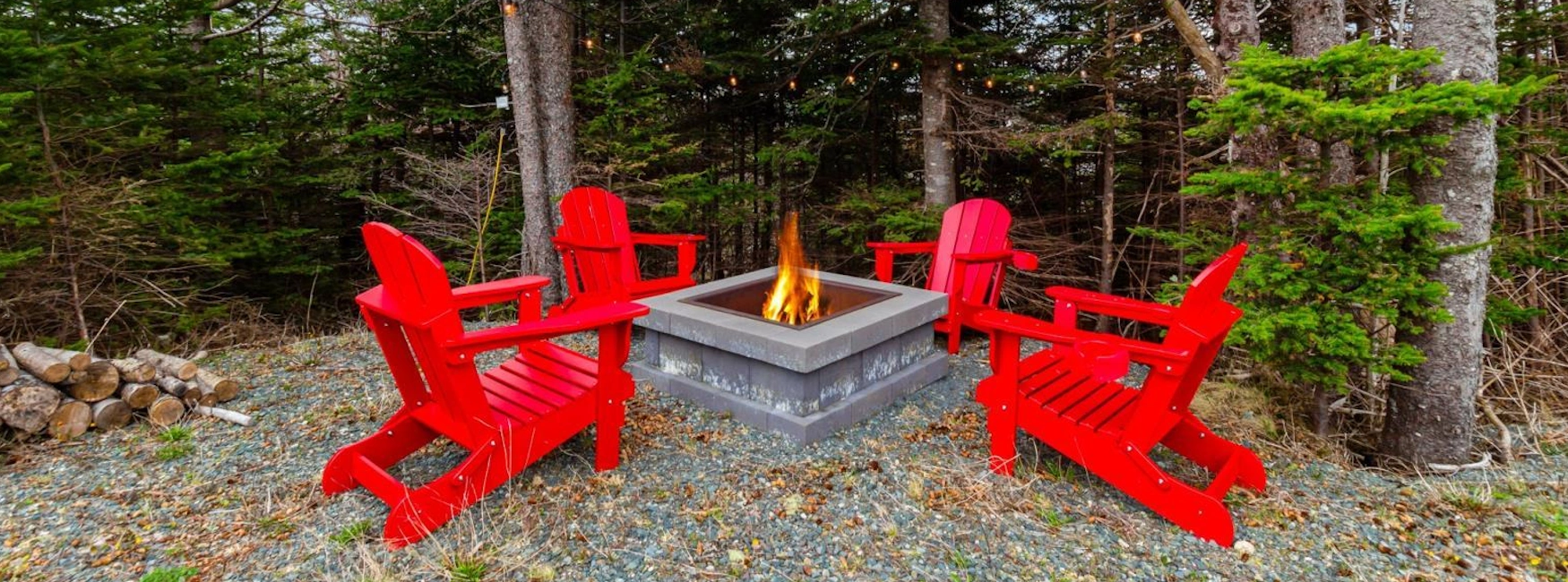 Outdoor fire pit area surrounded by red Adirondack chairs and lush trees in Portugal Cove-St. Philip's