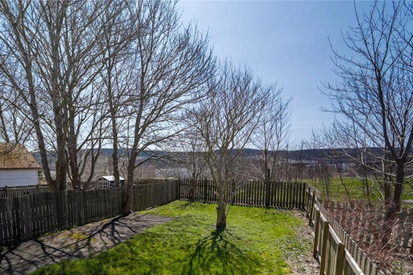 Fenced backyard in Buckmaster’s Circle with leaf-bare trees, green lawn and a distant view toward the water and hills.