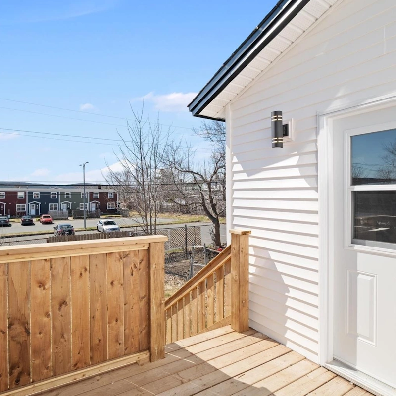 Sunny wooden deck and back entry of a Buckmaster’s Circle home, with colourful row houses and parked cars visible across the street.