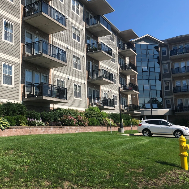 Modern multi-story condo building featuring balconies, spacious green areas, landscaped gardens, and convenient parking—ideal for comfortable urban living.